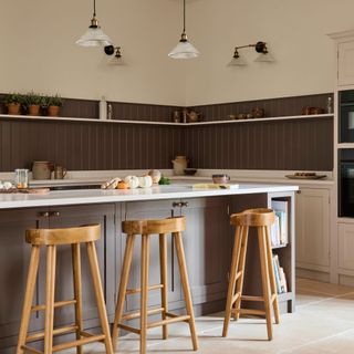 Brown and cream Shaker kitchen with large kitchen island and wooden bar stools and brown painted wood wall panelling