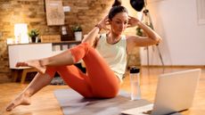 Woman exercising at home in front of a laptop on the floor