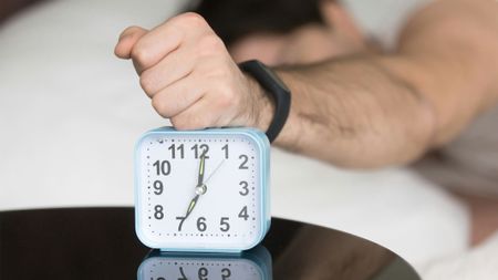 A man lying in bed with his fist on a clock.