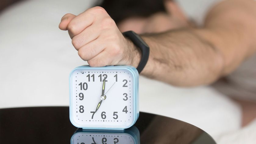 A man lying in bed with his fist on a clock.