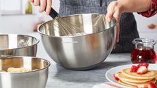 A set of three stainless steel KitchenAid mixing bowls being used in a kitchen to mix cake batter