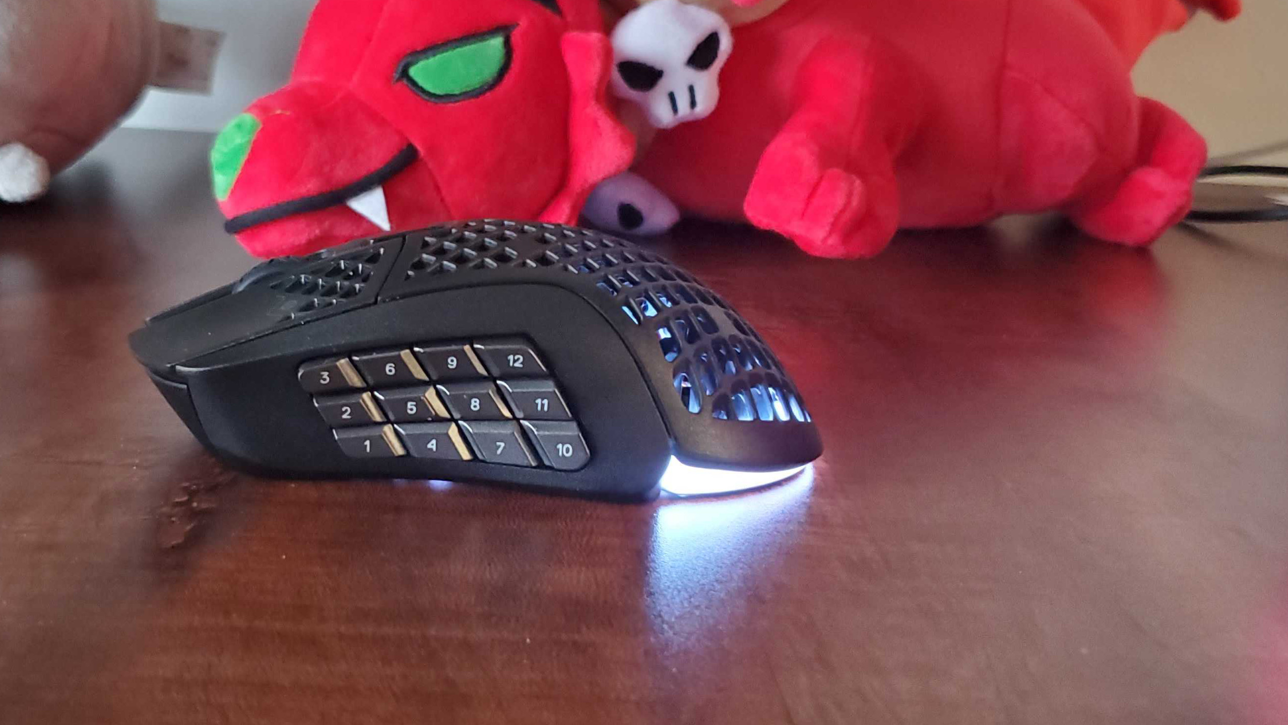 SteelSeries Aerox 9 on a dark wood desk next to some plushies