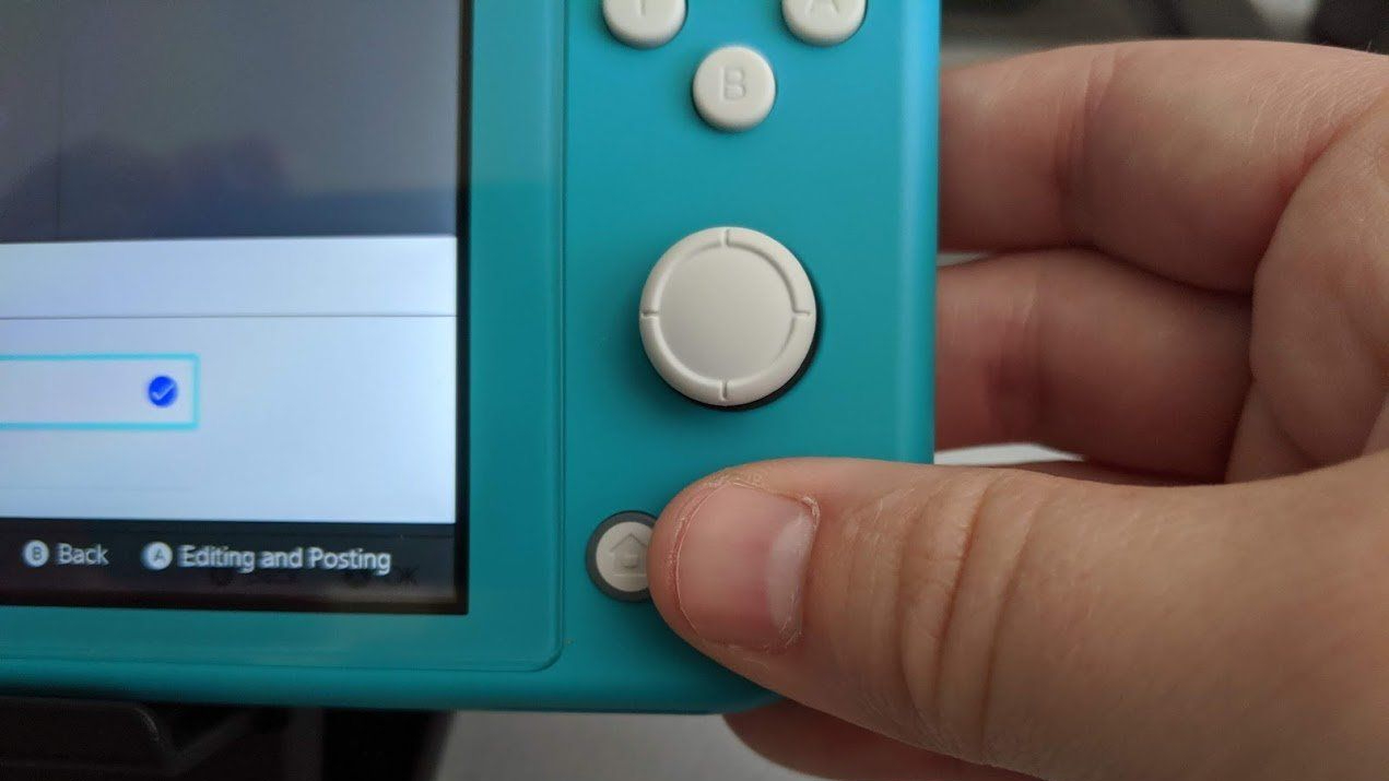 A thumb is seen on the home button of a Nintendo Switch