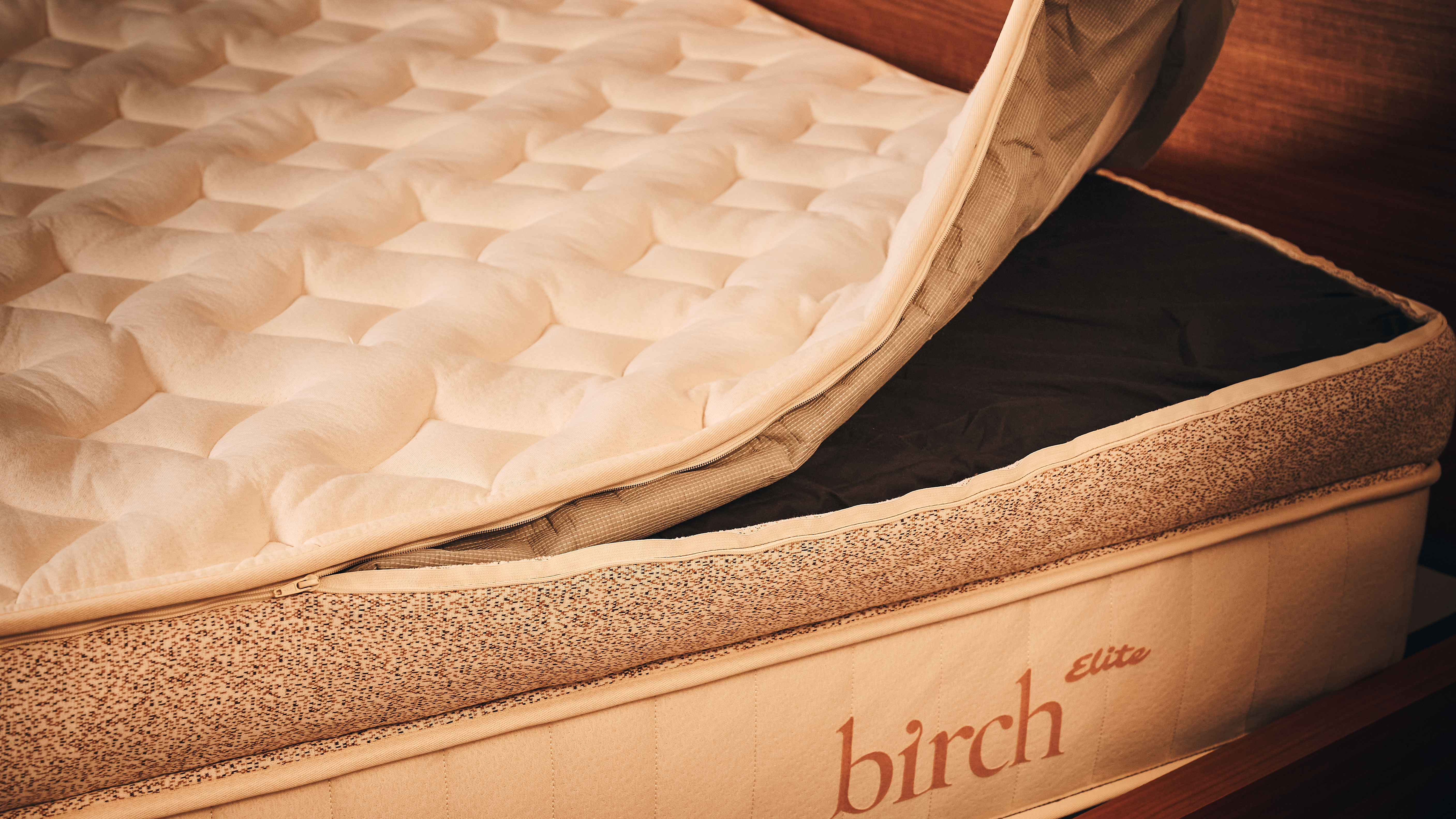 The image shows the beige and brown Birch Elite Natural mattress with its cover pulled back to reveal the latex layer insert