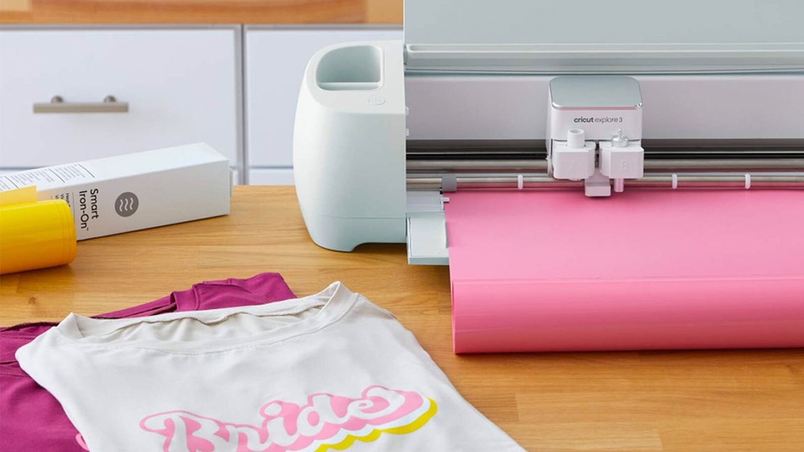 Best Cricut Explore 3 bundle deals; a digital craft machine next to some custom designed clothes