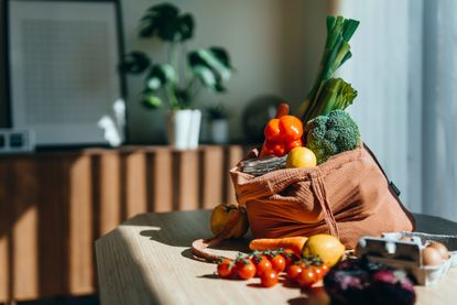 Eco-friendly reusable shopping bag with multi-coloured fresh vegetables and groceries on the table at home