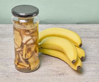 jar of banana peels in water next to bananas