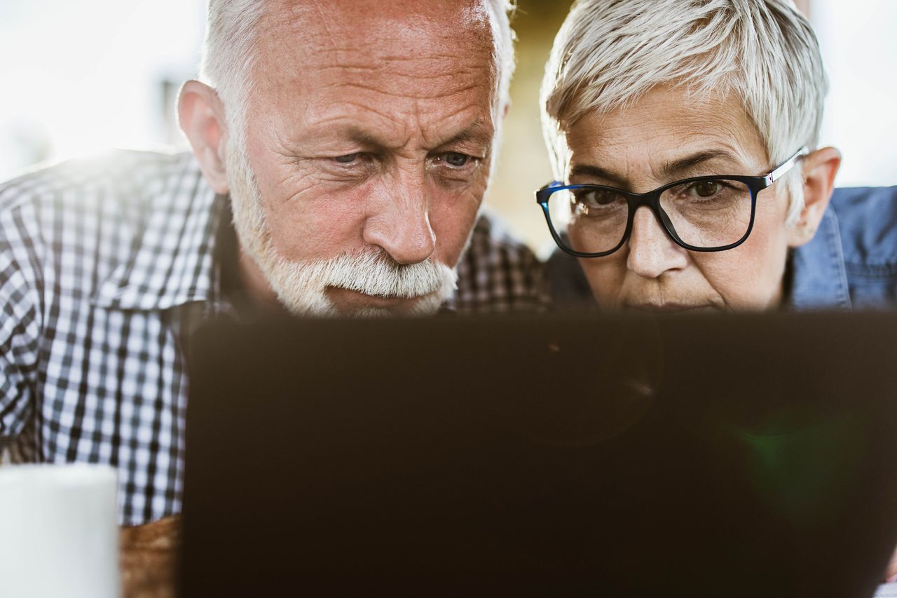 An older couple carefully examines information on a laptop.