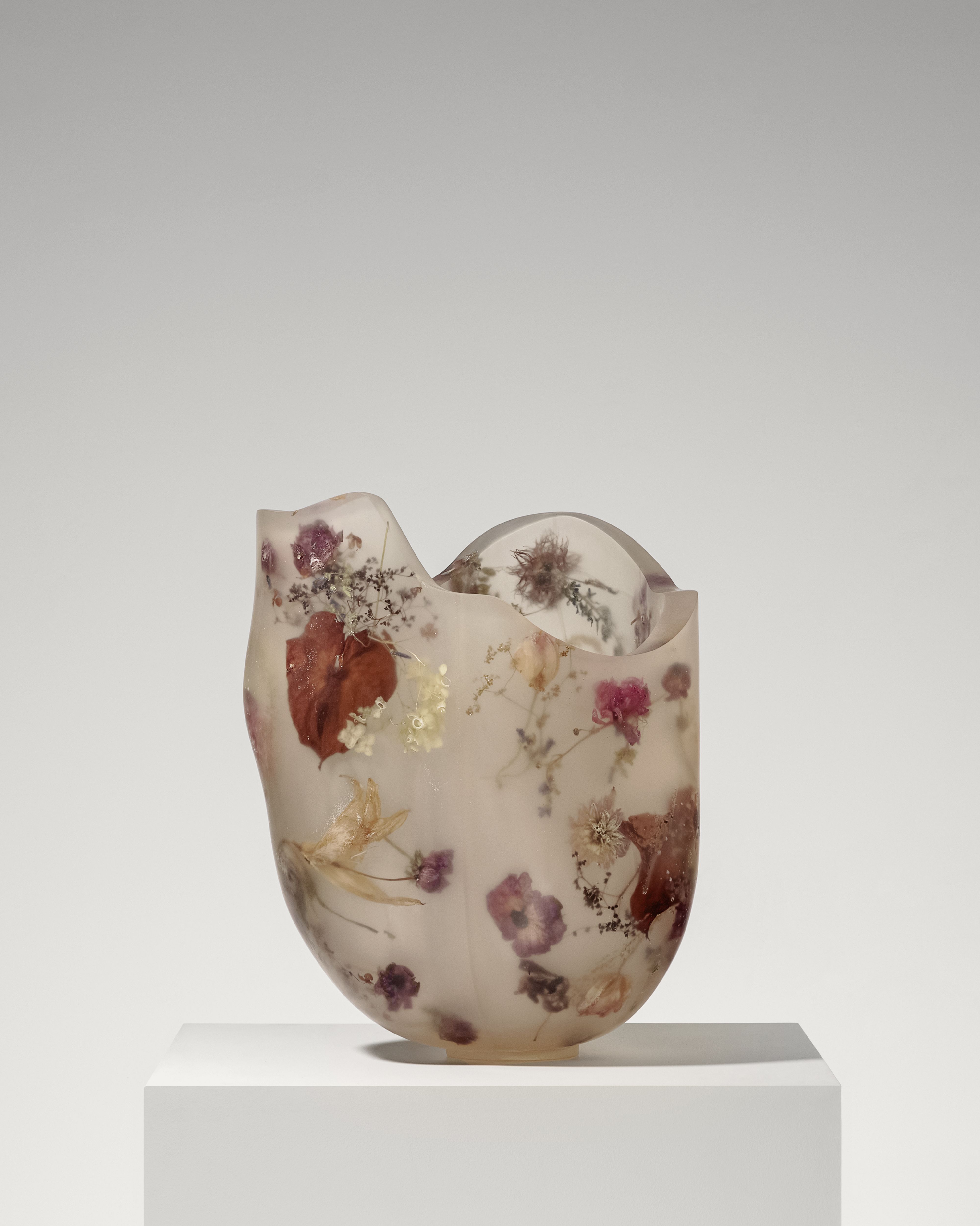 Furniture, lamps, and accessories featuring a resin body and encapsulated, frozen-in-time florals, petals, and vegetation in them, showcased in a brightly lit gallery setting.