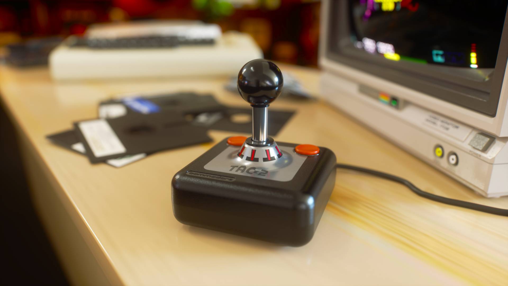 New TAC-2 joystick by Commodore on wood desk with C64 and monitor in backdrop.
