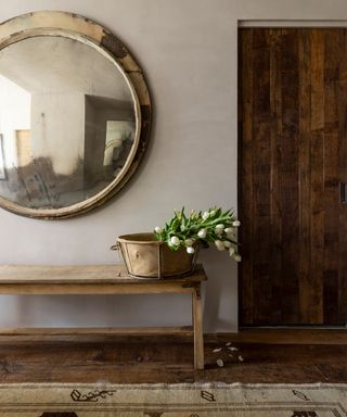 rustic entryway with limewashed walls, a reclaimed wood bench and large antique mirror with patina