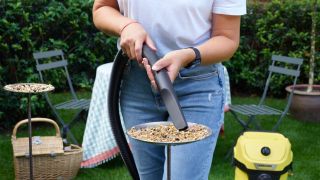 A woman using a Karcher WD3 to hoover up bird seed from a garden bird table