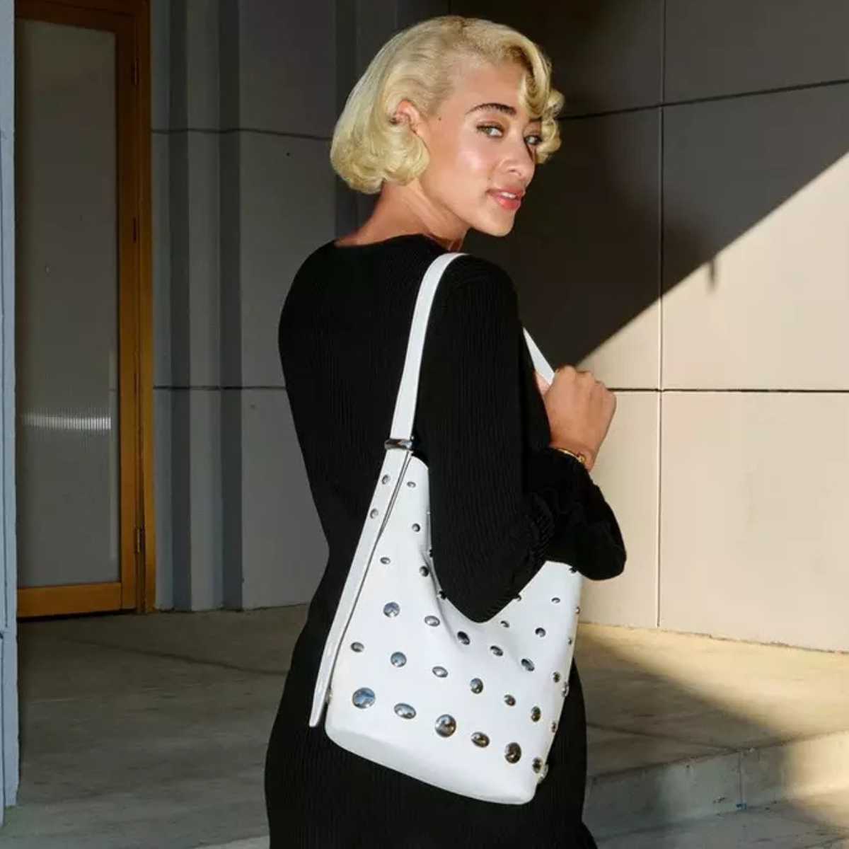 Woman wearing black top and white Kate Spade crossbody bag, with green charm.