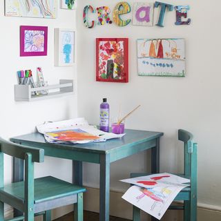 childrens bedroom with white wall and wooden craft table with wooden chair and crafts on wall