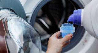 Woman pouring washing detergent into a container by the side of a washing machine drum