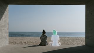 A woman sat next to her Replika avatar on a beach