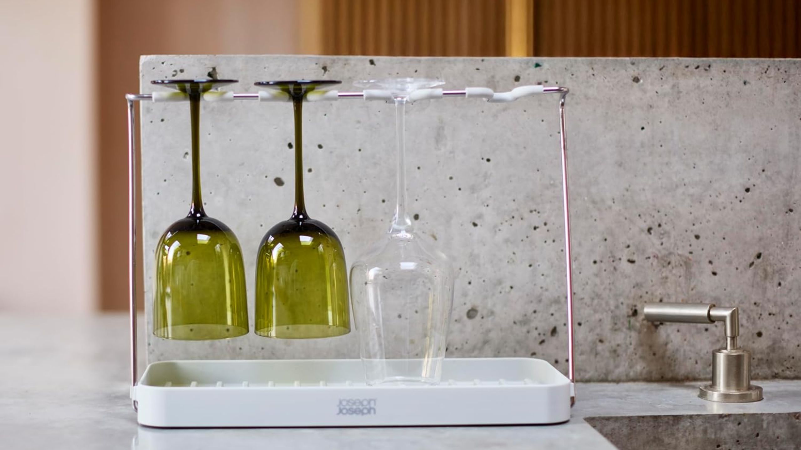 A wine glass drying rack with three wine glasses hanging from it beside a sink
