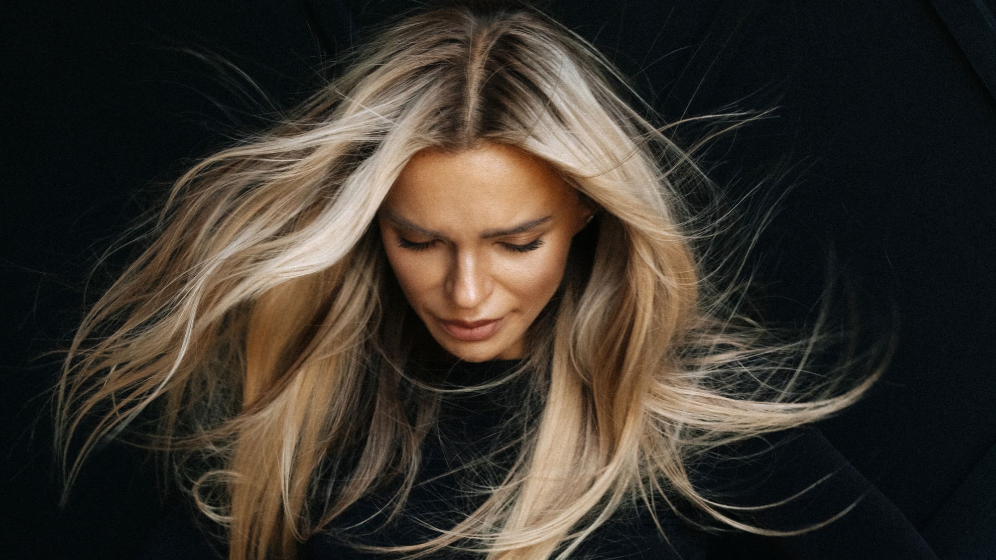 model with bright blonde hair and darker roots looking down at the floor on a black background - best root touch-ups
