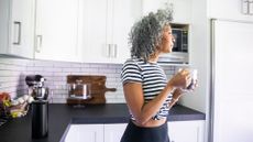 Woman wearing top and leggings standing in kitchen, holding mug of coffee, representing what to do after a bad night's sleep