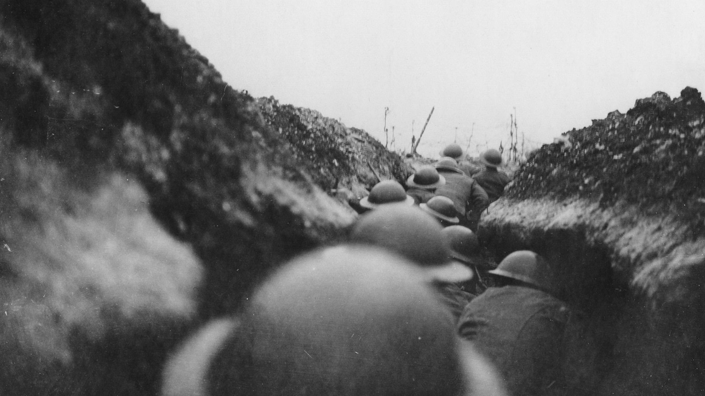 A black and white photo of British soldiers lined up in a narrow trench during WW1.