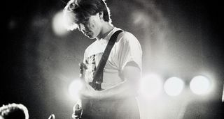 A black-and-white shot of Will Sergeant performing with Echo and the Bunnymen at the Royal Albert Hall in 1983, with white stage lights in the background.