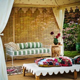 Moroccan style garden tent, sofa, cushions, rugs, low table/stool, elephant rattan table, vase of flowers