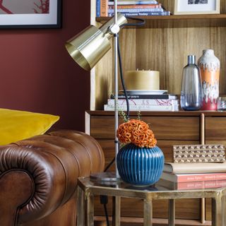 A brown leather sofa with a side table and a metallic gold reading lamp