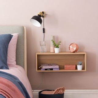 bedroom with pink wall and wooden shelg and bedside lamp