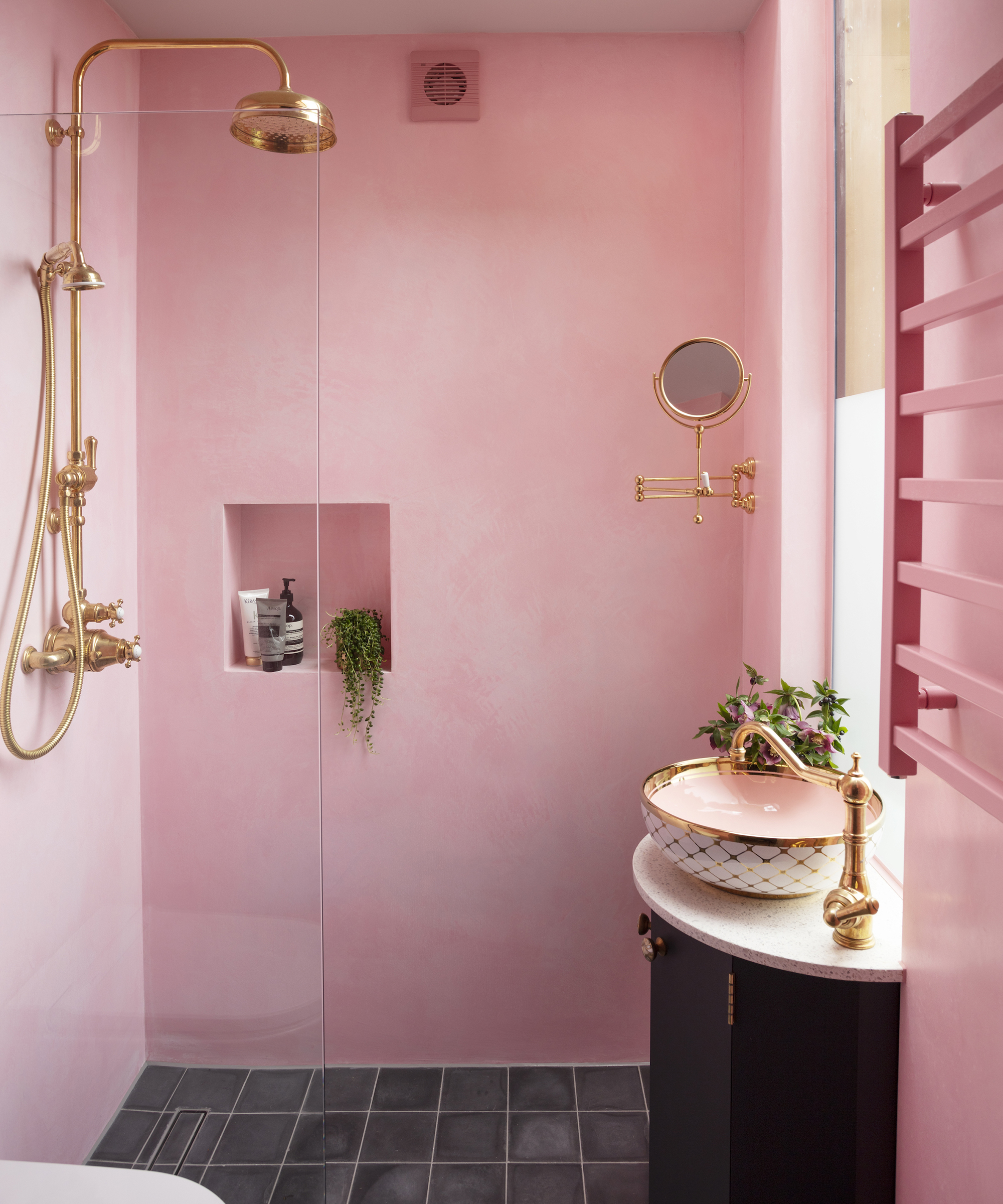 A pink shower enclosure with brass shower head and white and pink basin