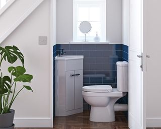 An under the stairs downstairs toilet with white toilet, blue half-tiled wall and corner vanity unit