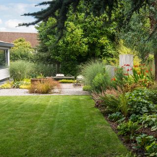 outdoor seating area beside a lawn with a corten steel round water feature, bench seating, wild grasses and a firepit