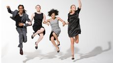 Four people dressed in business suits jump together enthusiastically.