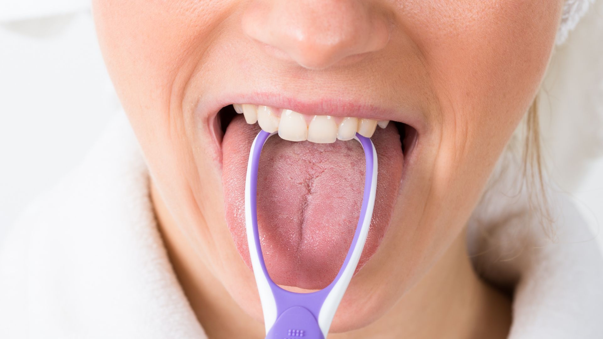 Mujer que usa un raspador de lengua morado para mostrar los beneficios de rasparse la lengua