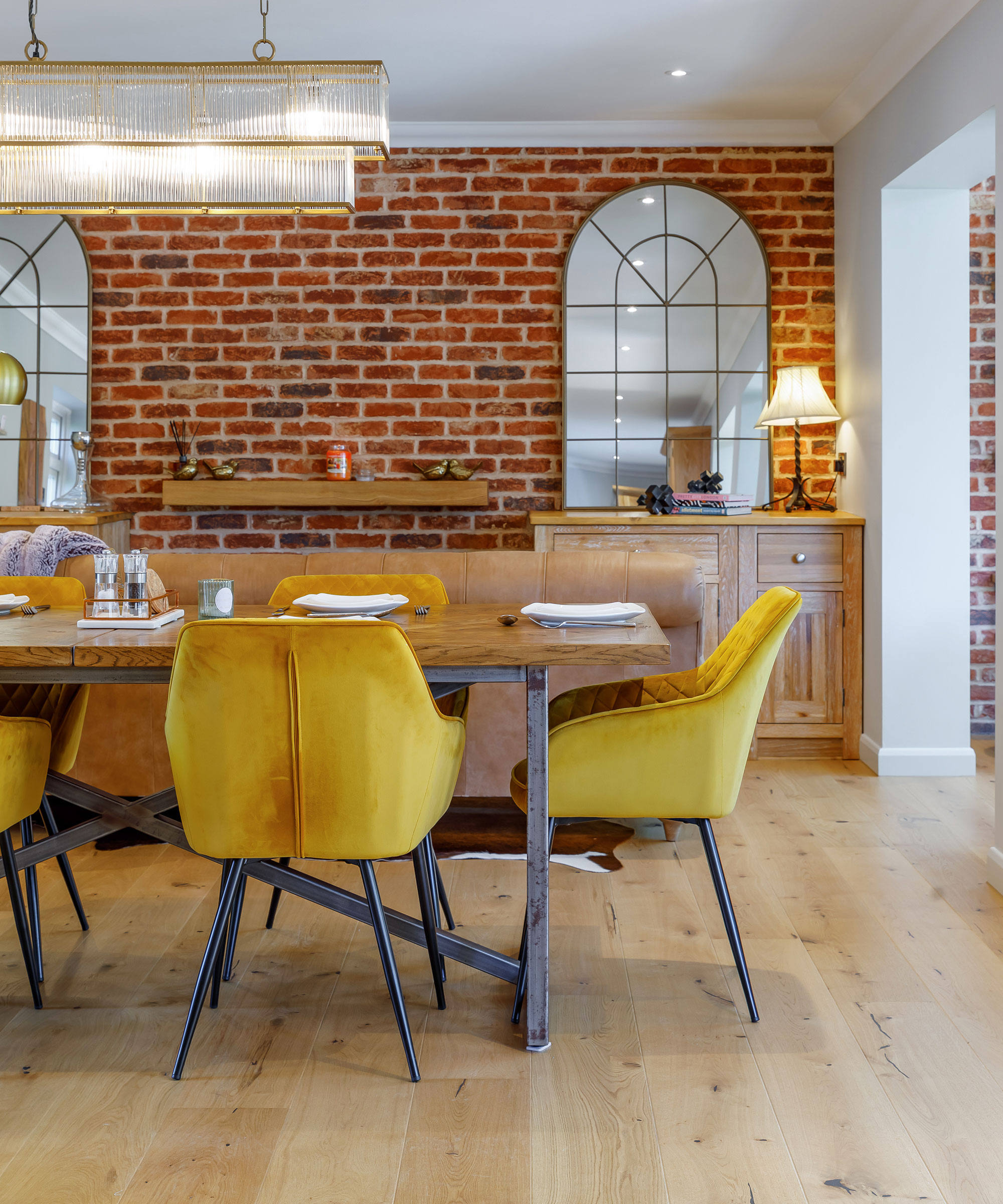wide engineered flooring in dining room with yellow dining chairs and exposed brick wall
