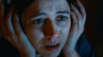 A close up of Evy holding her hands over her headphones in A24 horror film Undertone