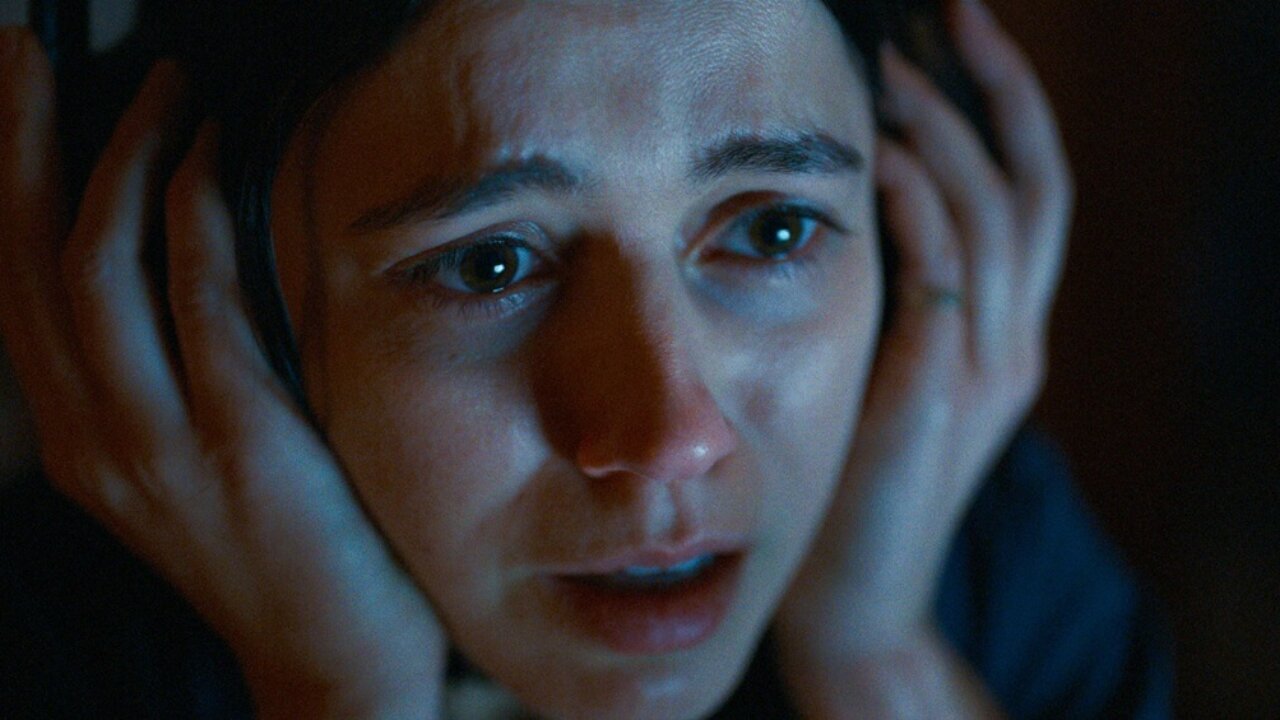 A close up of Evy holding her hands over her headphones in A24 horror film Undertone
