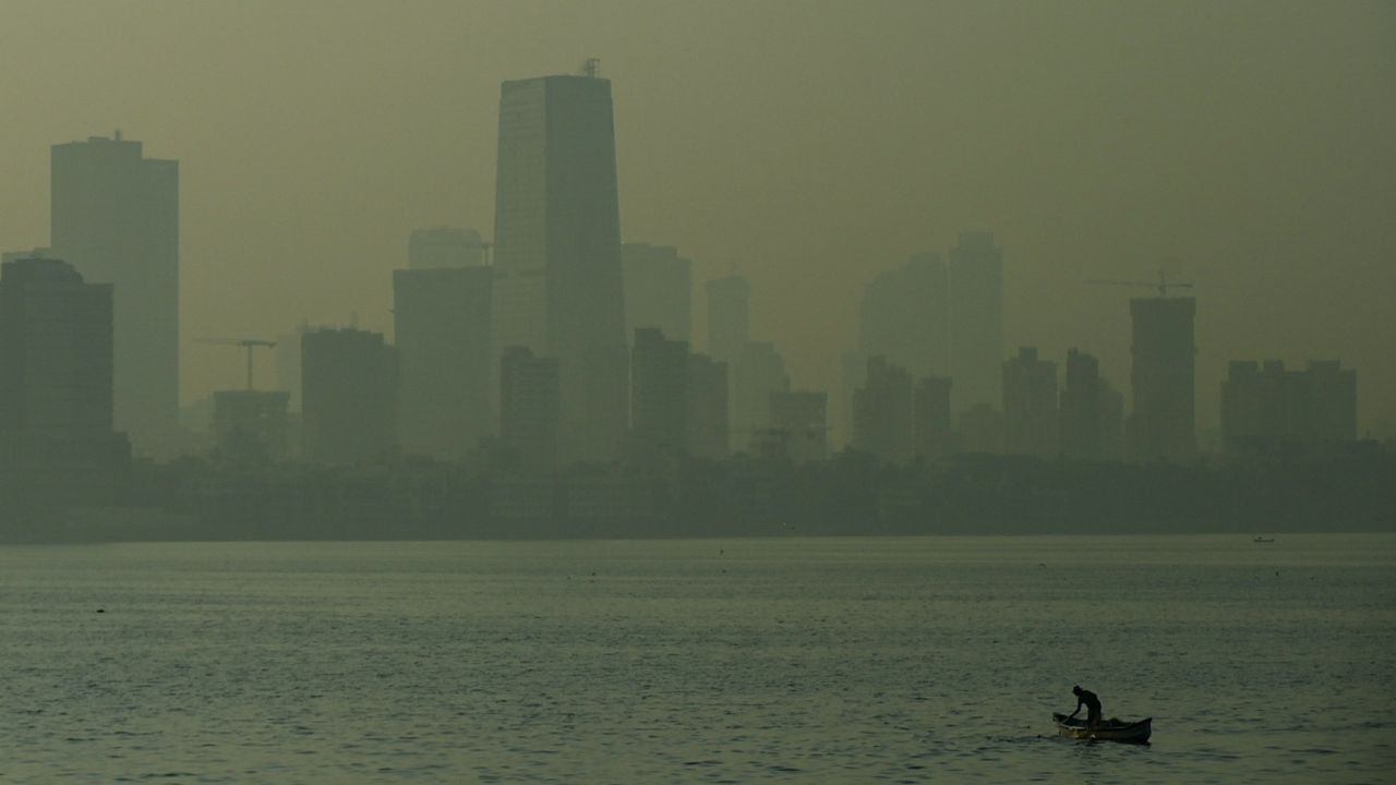 A fisherman steers his boat in front of the city skyline on a polluted morning in Mumbai