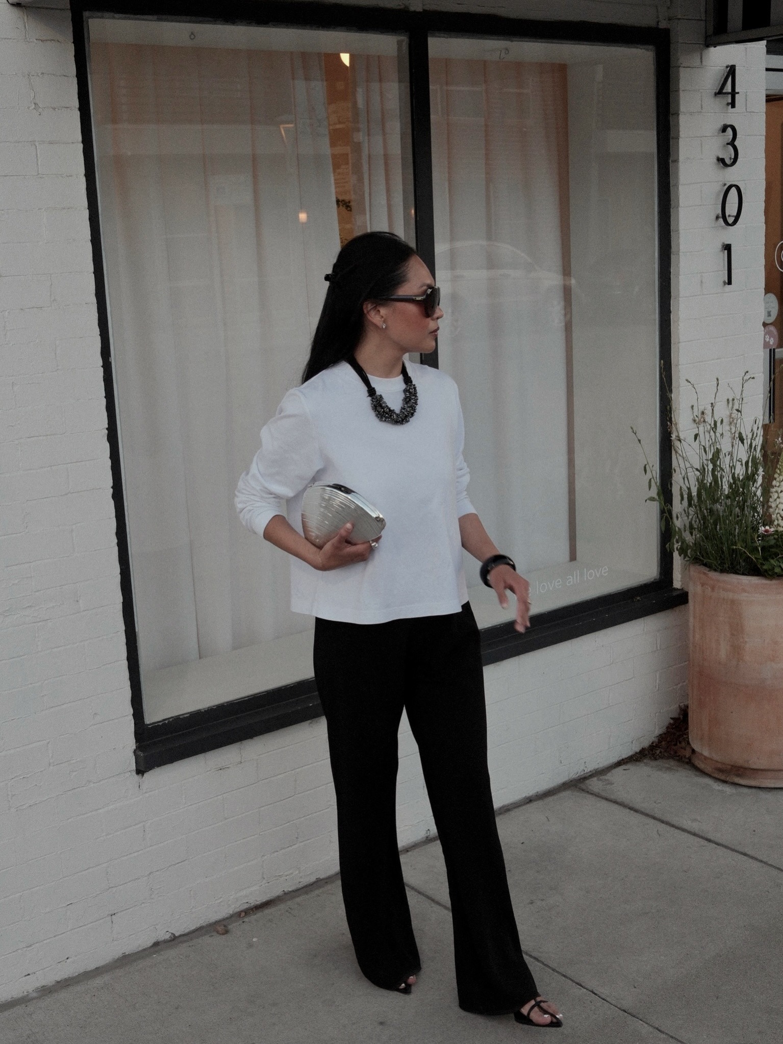 Woman wears white long sleeve top, black trousers and necklace