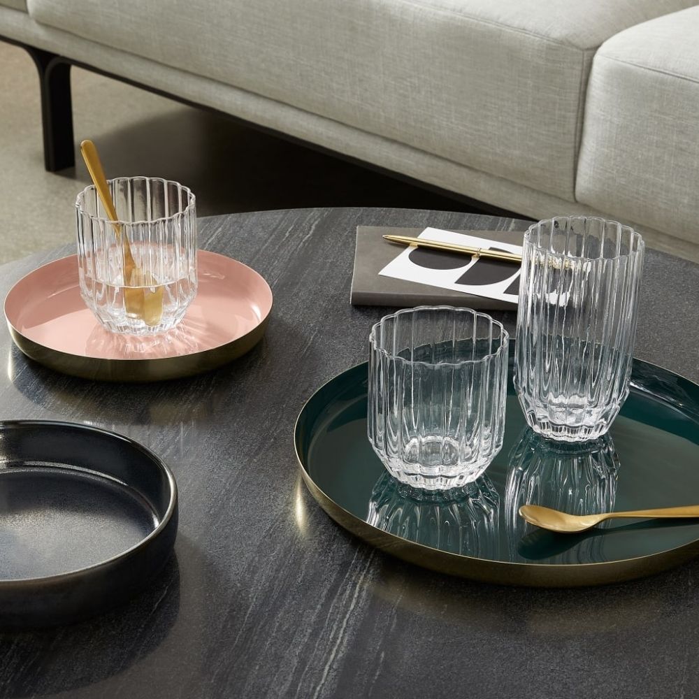 2 brass serving trays with glasses on top of round wooden table next to white couch