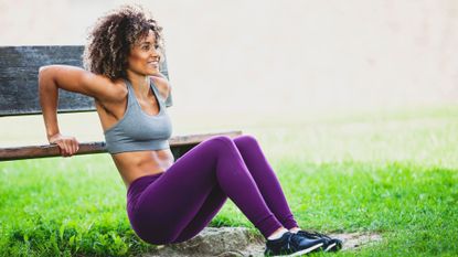 A woman performing triceps dips on a bench in a park