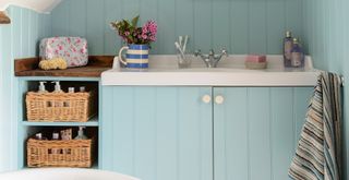 Blue bathroom with wood paneling and vanity unit with baskets for storage to show a spring cleaning tip for small spaces and apartments