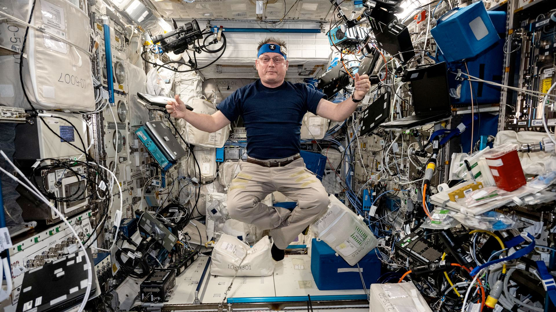 a man in a dark blue t-shirt and khaki slacks floats in the middle of a space station module