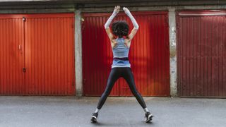 Young fit female doing jumping jacks in front of red garage doors photographed from behind