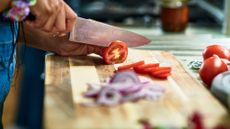 side shot of someone slicing roma tomatoes with a chef's knife