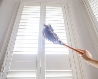 Person cleaning the shutters with a feather duster while light creeps in through the gaps