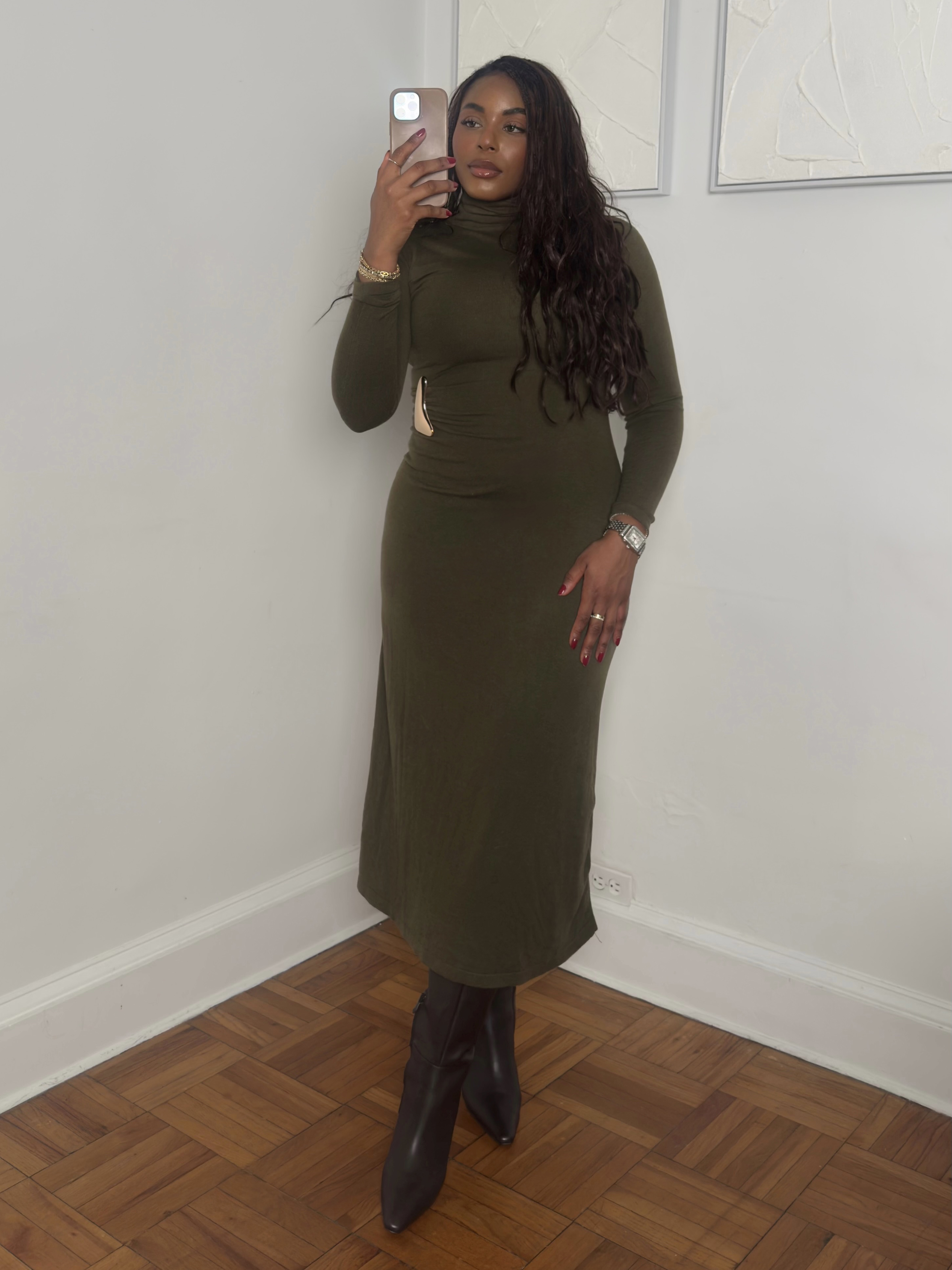 fashion and beauty influencer Kaye Bassey poses in a winter 2026 outfit formula with a green turtleneck dress with a gold brooch and knee-high boots