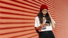 woman texting with surprised look on her face while outside against a red wall