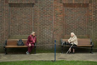 Two women keep 6 feet (1.8 meters) apart as they speak to each other from adjacent park benches amidst the novel coronavirus COVID-19 pandemic, in the centre of York, northern England on March 19, 2020.