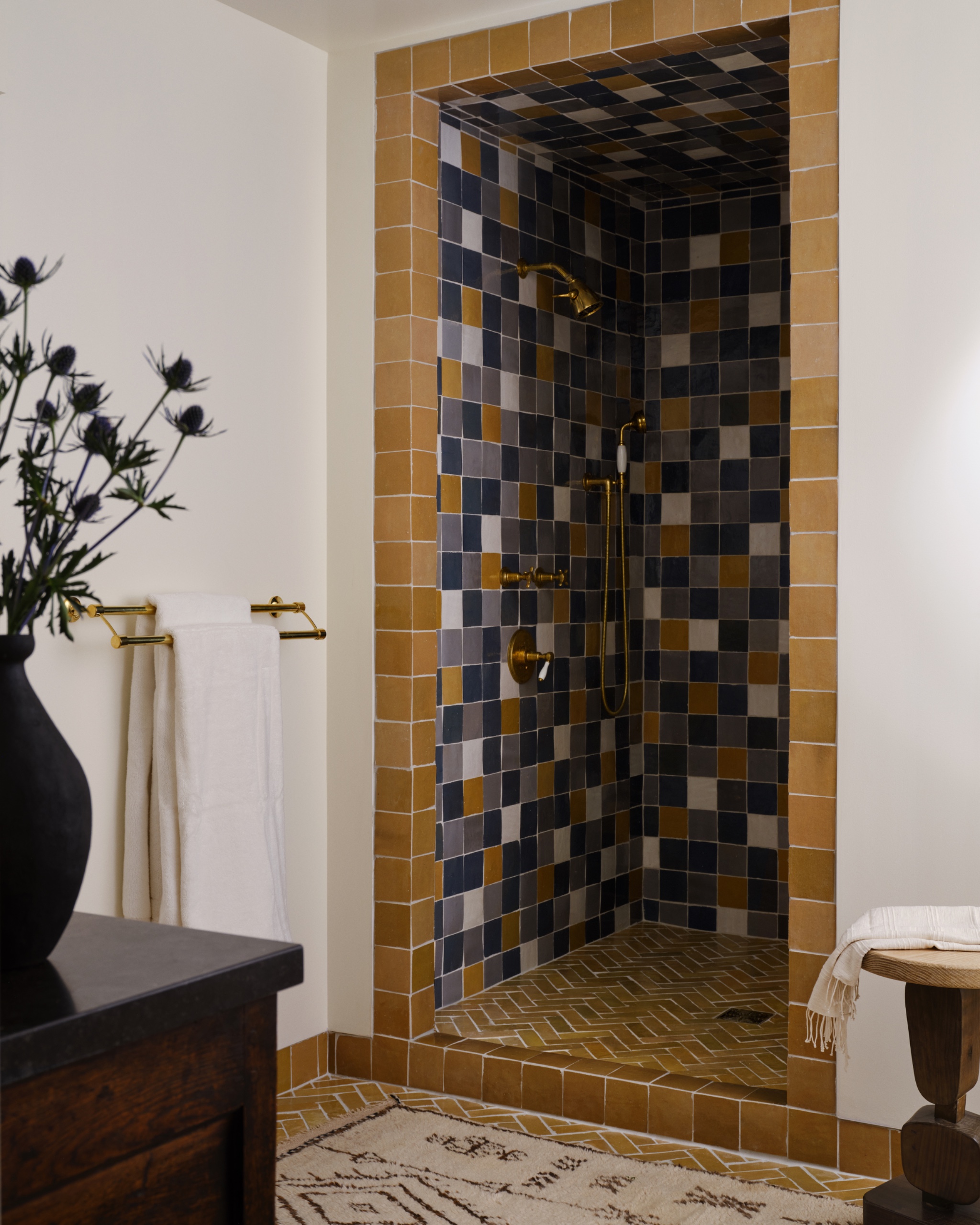 Shower framed in mustard tiles, with blue, gray, cream and mustard zellige walls and ceiling, a herringbone tile floor and brass fixtures.