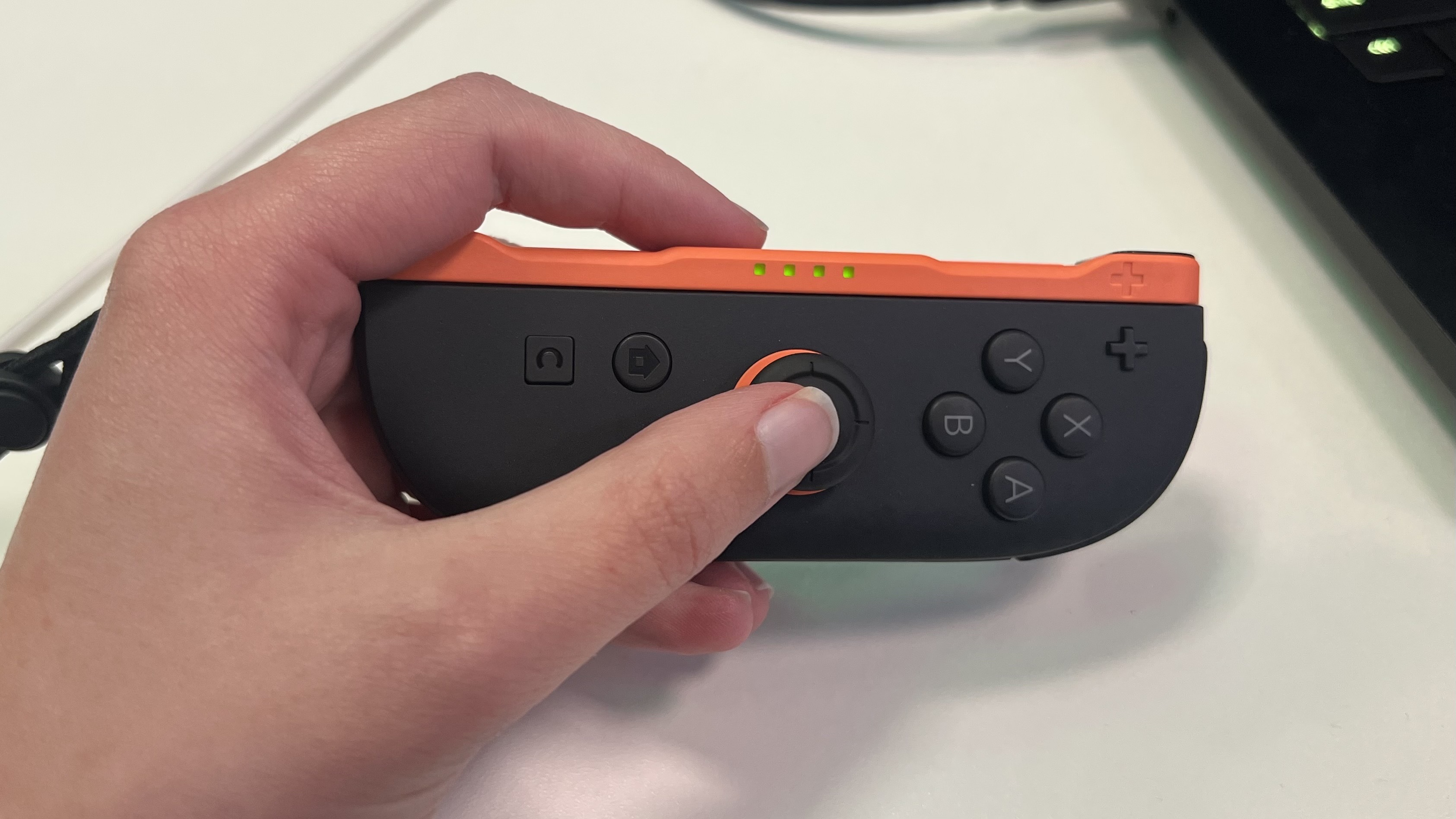 Hand holding right Nintendo Switch 2 Joy-Con controller with thumb extended to reach the thumbstick